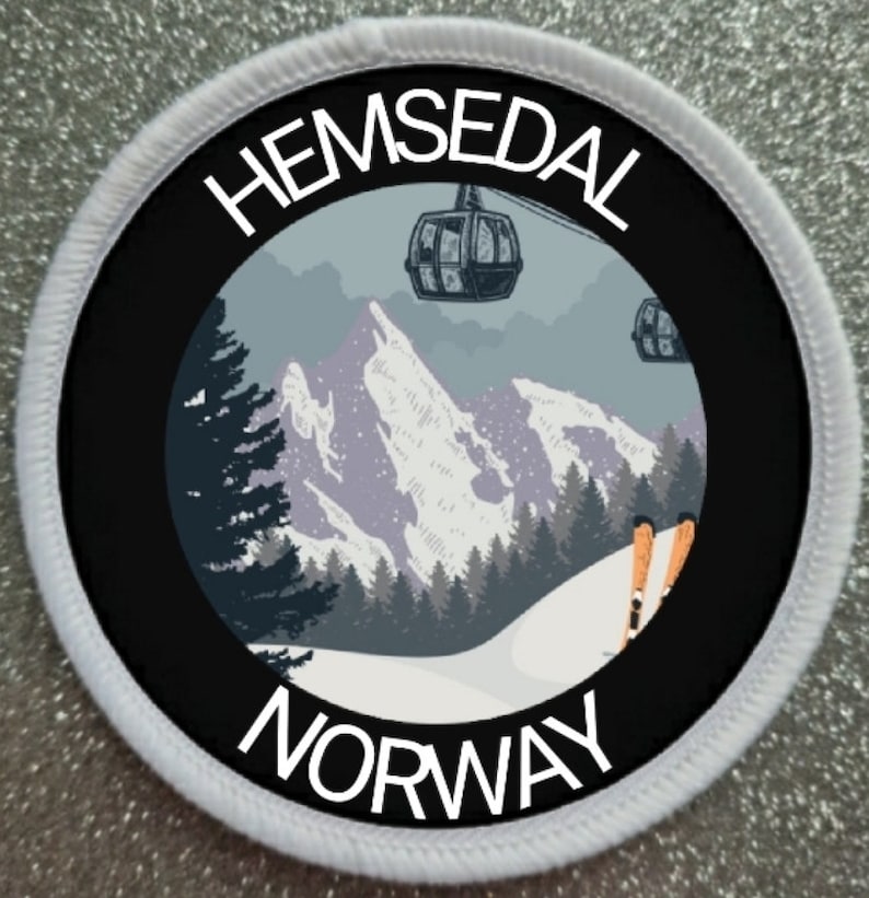 K&ouml;nnte beinhalten: Ein runder bestickter Aufn&auml;her mit wei&szlig;em Rand, der eine Berglandschaft, Skilift-Gondeln und orangefarbene Skier zeigt. Der Text Hemsedal ist oben in Wei&szlig; und Norway unten in Wei&szlig; auf schwarzem Hintergrund aufgedruckt.