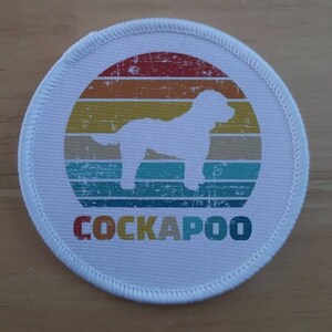 May include: White round patch with a vintage-style sunset graphic and a silhouette of a Cockapoo dog. The text "COCKAPOO" is printed in colorful letters below the graphic.