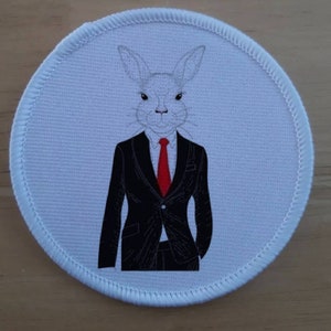 Puede incluir: Un conejo blanco con un traje negro y una corbata roja. El conejo está representado en un estilo de dibujos animados y tiene una expresión seria.
