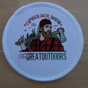 May include: White round patch with a red and black lumberjack illustration holding an axe. The text "LUMBERJACK SHOW" is in red and black with "Est. 1988" below. The text "The GREAT OUTDOORS" is in green and red.