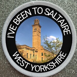 May include: A white round patch with black text that reads "I've Been To Saltaire West Yorkshire". The patch features a photo of a tall brick building with a clock tower.