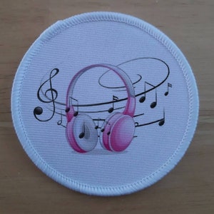 May include: A white round patch with a pink and gray pair of headphones with musical notes in the background.