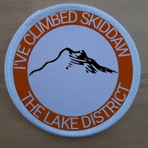 May include: White round patch with an orange border. The text "I've Climbed Skiddaw The Lake District" is printed in a circle around a black silhouette of a mountain.