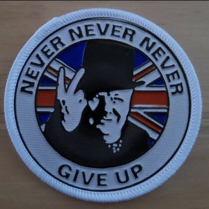 May include: A circular patch with a white border features the words "NEVER NEVER NEVER GIVE UP" in black. The center depicts a silhouette of a man in a top hat giving a peace sign, with a Union Jack flag design in the background.