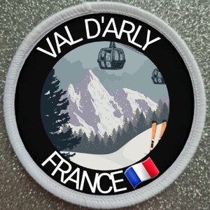 Könnte beinhalten: Runder Aufnäher mit dem Text "VAL D'ARLY FRANCE", der eine Berglandschaft mit einer Seilbahn und der französischen Flagge umrahmt. Der Aufnäher hat einen schwarzen Rand und einen weißen, genähten Rand.