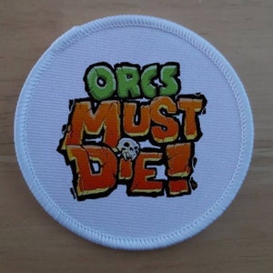 May include: White round patch with a green, orange, and white graphic that says "Orcs Must Die!"