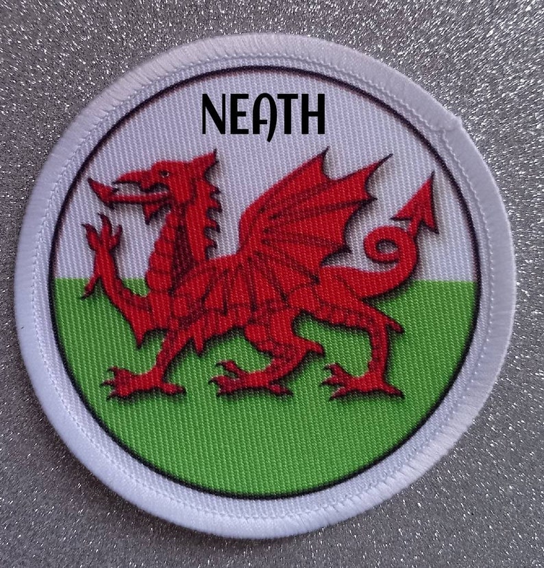 May include: A white circular patch with a red dragon on a green and white background. The text "NEATH" is printed in black at the top of the patch.