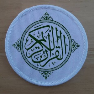 Op de afbeelding: Ronde witte patch met een groen geborduurd ontwerp van de islamitische zin "Allah" in Arabisch schrift. Het ontwerp is omgeven door een decoratieve rand.