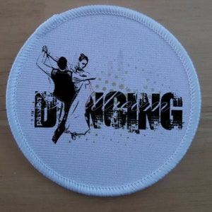 May include: White round patch with a black and white image of a couple ballroom dancing. The text "passion" and "dancing" are in black with a white background.