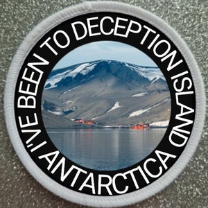Puede incluir: Un parche redondo blanco con un círculo negro en el centro. El círculo negro tiene texto blanco que dice "I've Been to Deception Island Antarctica". Dentro del círculo negro hay una foto de una cordillera con nieve en las cumbres y una masa de agua en primer plano.