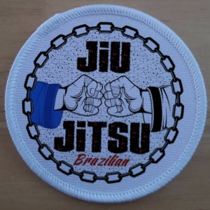Puede incluir: Parche redondo blanco con un borde de cadena negro. En el centro, una ilustración en blanco y negro de dos manos que se dan la mano, con el texto "Jiu Jitsu Brazilian" en negro y rojo.