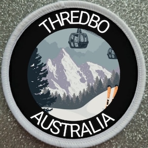 Puede incluir: Un parche circular blanco y negro con el texto "THREDBO AUSTRALIA" y un gráfico de una escena de montaña nevada con remontes y esquiadores.