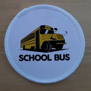 May include: Circular white patch featuring a yellow school bus illustration and the words "SCHOOL BUS" in black. The bus has black wheels, windows, and detailing. The patch is edged with a stitched white border.