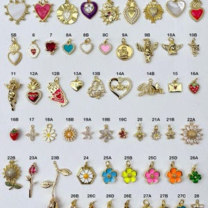 May include: Assortment of 28 gold-tone charms with various designs, including hearts, flowers, religious symbols, and letters. The charms are arranged in rows on a white background.