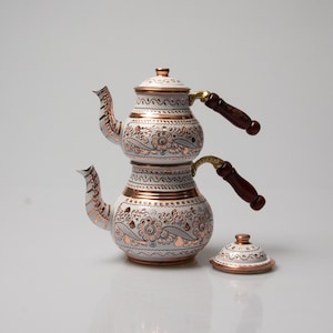 Peut inclure: Service à thé turc en cuivre et blanc avec des motifs floraux complexes. L'ensemble comprend une théière avec un couvercle et deux pots séparés pour infuser le thé.