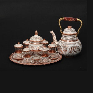 Peut inclure: Un service à thé turc en cuivre et blanc avec une théière, un sucrier et six tasses et soucoupes. L'ensemble est décoré de motifs floraux en cuivre.