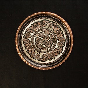 Puede incluir: Una bandeja redonda de cobre con fondo negro y diseños florales intrincados en cobre.