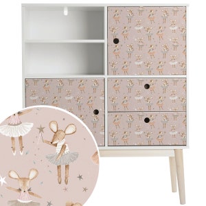 Peut inclure: Armoire blanche avec quatre tiroirs et une étagère. Les tiroirs et les portes de l'armoire sont décorés d'un motif rose et marron de souris portant des tutus et tenant des baguettes.