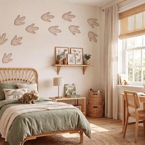 Könnte beinhalten: Ein Schlafzimmer mit einem Rattan-Bettgestell, salbeigrüner Bettwäsche, einem Triceratops-Plüschtier und einem Nachttisch aus Holz mit Lampe. An der Wand befinden sich beige Dinosaurier-Fußabdruck-Aufkleber und ein Holzregal mit gerahmter Kunst.
