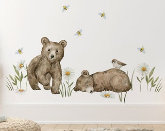 May include: Two brown bear cubs, one standing and one sleeping, surrounded by white daisies and green grass. There are also several blue and yellow bees flying around the bears.