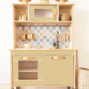 May include: A wooden toy kitchen playset with a light brown finish. The kitchen features a pretend oven, a sink with a black faucet, and two cabinets with leather handles. The backsplash is a checkered pattern with floral accents.