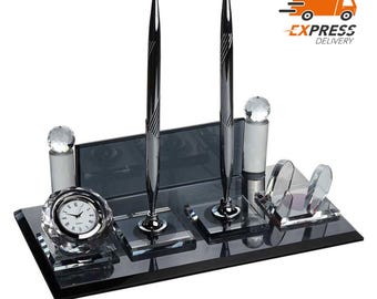 Könnte beinhalten: Ein schwarzer Glas-Schreibtisch-Organizer mit zwei silbernen Stiften, einer Uhr und Kristall-Akzenten.