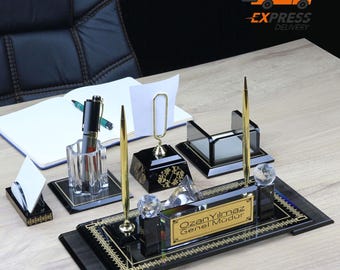 Könnte beinhalten: Schwarzes Schreibtisch-Organizer-Set mit goldenen Akzenten. Enthält einen Stifthalter, einen Visitenkartenhalter, einen Notizhalter und ein Namensschild mit der Aufschrift "Ozan Yilmaz Genel Mudur".