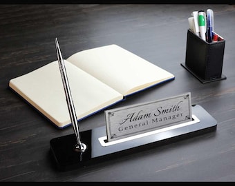 May include: Black desk organizer with a silver pen holder and a silver nameplate that reads "Adam Smith General Manager".