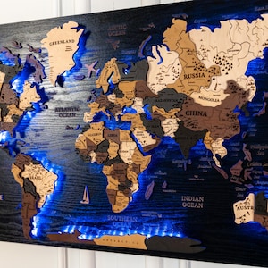 May include: A wooden world map with a black background and various shades of brown continents. The map is illuminated with blue LED lights, and includes small sailboat and airplane cutouts. The map is mounted on a wall.