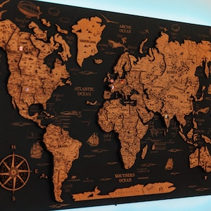 以下が含まれることがあります： 黒い背景にコルク製の地球儀の地図。左下にコンパスがある。地図は後ろから青い光で照らされている。地図には様々な場所にピンが刺さっている。