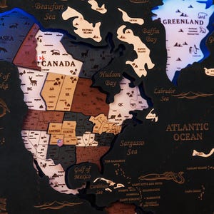 May include: A detailed wooden world map, highlighting North America. The map uses various colours and textures, with the United States, Canada, and Greenland clearly visible. The Atlantic Ocean is labelled, and the map includes detailed geographical features.