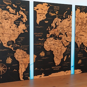 May include: A three-panel wooden world map with a black background and detailed, light brown continents. The map includes oceans, seas, and compass rose details. Decorative elements include ships and aircraft. The panels are mounted on a wooden surface.