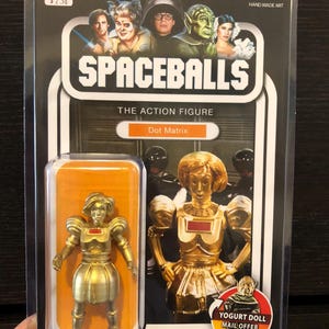 May include: A gold-colored action figure of Dot Matrix from the movie Spaceballs. The figure is packaged in a retro-style box with a picture of the character on the front. The box also includes the text "Spaceballs: The Action Figure" and "Dot Matrix".