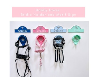 May include: Four colorful hobby horse bridle holders with personalized nameplates: Quincy, Peaches, Delwyn, and Finn. Each holder features a different design, including a star, crown, heart, and horse silhouette. The holders are mounted on a white wall.