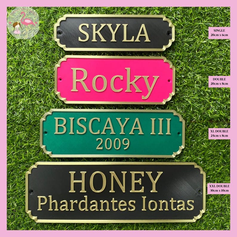 May include: Four personalized horse stall nameplates with gold lettering. The top nameplate is black with the name "SKYLA" in gold lettering. The second nameplate is pink with the name "Rocky" in gold lettering. The third nameplate is green with the name "BISCAYA III 2009" in gold lettering. The bottom nameplate is black with the name "HONEY Phardantes Iontas" in gold lettering. Each nameplate has a gold border and a different size.