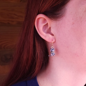 May include: A dangling earring featuring a small, spherical knot design crafted from thin, intertwined navy blue and white cord, accented with metallic gold wire, suspended from a simple gold-toned metal hook wire.