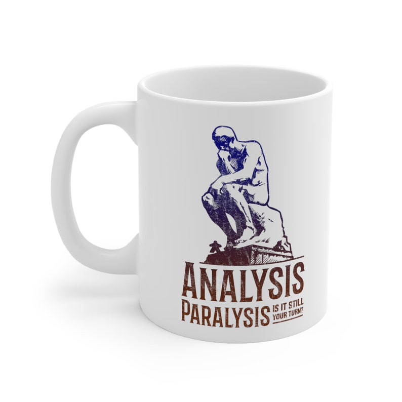 Pu&ograve; includere: Tazza in ceramica bianca con un'illustrazione blu e bianca della statua del "Pensatore". Il testo "Analysis Paralysis Is It Still Your Turn?" &egrave; stampato in marrone e rosso sulla tazza.