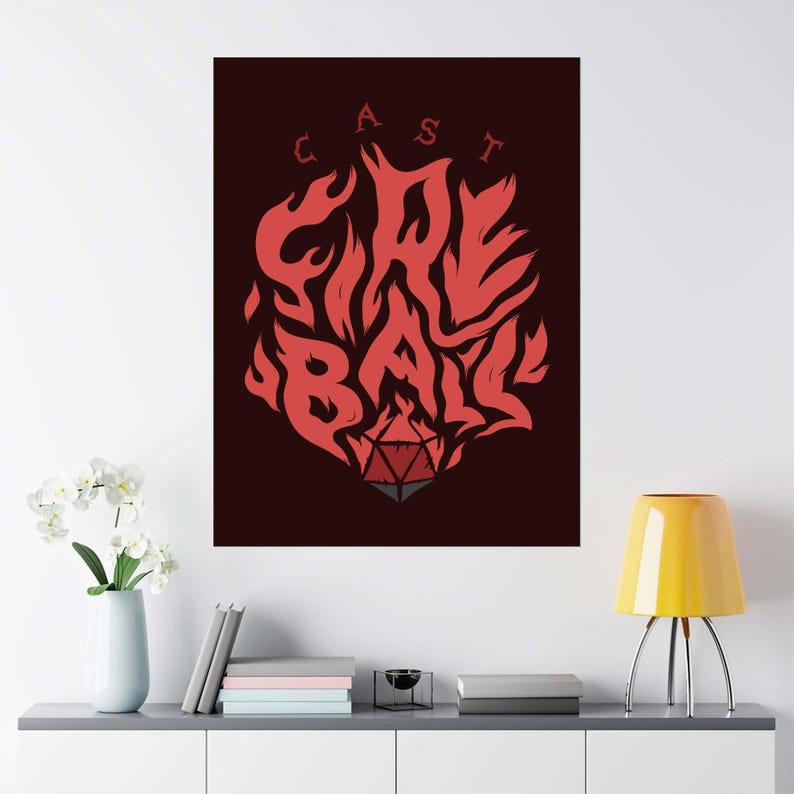 以下が含まれることがあります： 「CAST FIRE BALL」の文字が炎のデザインで描かれた赤と黒のポスター。炎の下部には赤とグレーのD20サイコロがあります。ポスターは白い壁に飾られています。