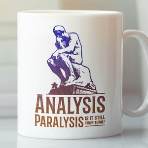 Puede incluir: Taza de cerámica blanca con una ilustración azul y morada de la estatua del "Pensador". El texto "Analysis Paralysis Is It Still Your Turn?" está impreso en marrón en la taza.
