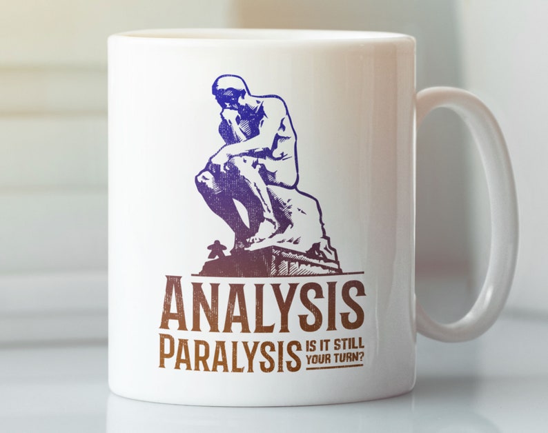 Pu&ograve; includere: Tazza in ceramica bianca con un'illustrazione blu e viola della statua del "Pensatore". Il testo "Analysis Paralysis Is It Still Your Turn?" &egrave; stampato in marrone sulla tazza.