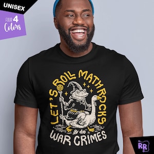 May include: Black unisex t-shirt with a whimsical graphic of a frog wizard riding a goose, with the text "Let's Roll Math Rocks & do War Crimes" in yellow. The shirt also has a "Four Colors" label.