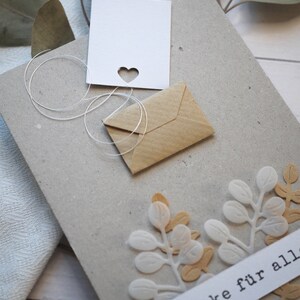 May include: A handmade greeting card with a heart-shaped cutout and a small kraft paper envelope. The card features white and tan leaf embellishments and the German text "danke f&uuml;r alles".