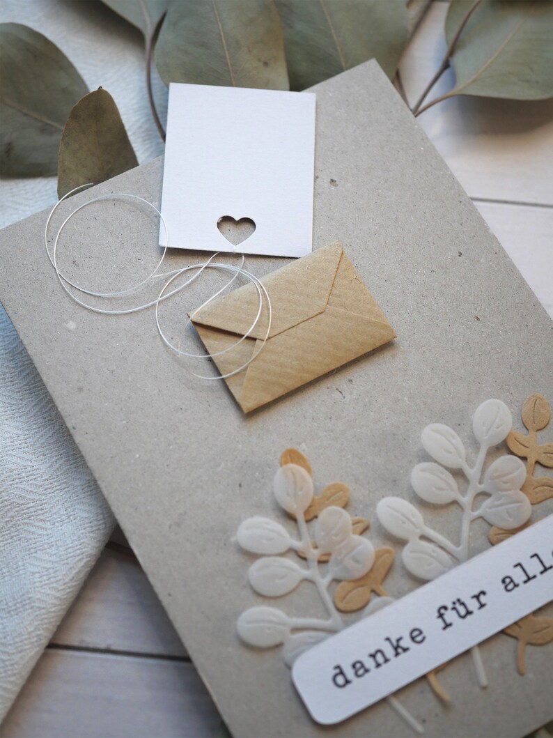 May include: A handmade greeting card with a heart-shaped cutout and a small kraft paper envelope. The card features white and tan leaf embellishments and the German text "danke f&uuml;r alles".