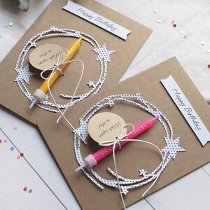 May include: Two brown card birthday cards with white paper cutouts of stars and a crescent moon. Each card has a small tag that says "Wish upon a star" and a small birthday candle.