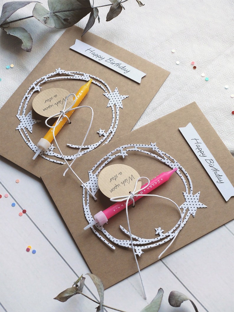 May include: Two brown card birthday cards with white paper cutouts of stars and a crescent moon. Each card has a small tag that says "Wish upon a star" and a small birthday candle.