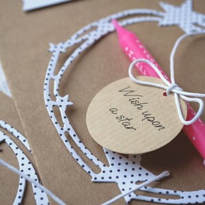 May include: A brown card with white polka dots and a white string tied around a circle tag that says "Wish upon a star". A pink candle is tied to the string.
