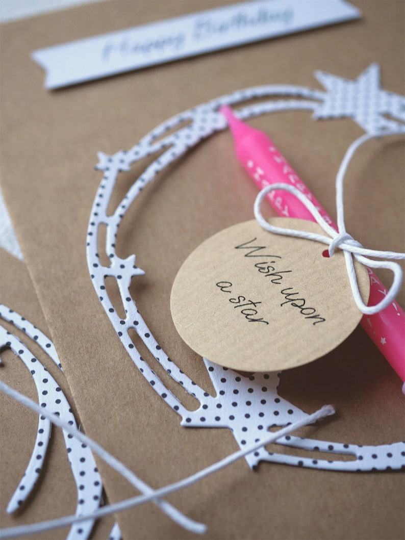 May include: A brown card with white polka dots and a white string tied around a circle tag that says "Wish upon a star". A pink candle is tied to the string.