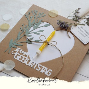 Puede incluir: Una tarjeta marr&oacute;n con un coraz&oacute;n blanco recortado. El coraz&oacute;n tiene una vela amarilla dentro. La tarjeta dice "zum Geburtstag" y "Kartenformat 15 x 15 cm". Hay una peque&ntilde;a etiqueta que dice "Wunscherf&uuml;ller: Kerze anz&uuml;nden & auspusten!"