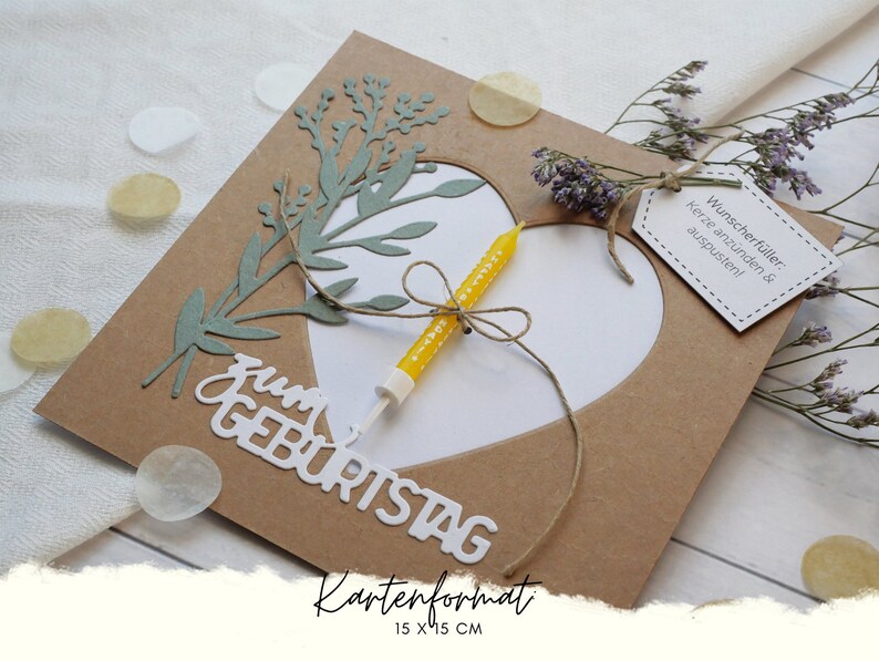 Puede incluir: Una tarjeta marr&oacute;n con un coraz&oacute;n blanco recortado. El coraz&oacute;n tiene una vela amarilla dentro. La tarjeta dice "zum Geburtstag" y "Kartenformat 15 x 15 cm". Hay una peque&ntilde;a etiqueta que dice "Wunscherf&uuml;ller: Kerze anz&uuml;nden & auspusten!"