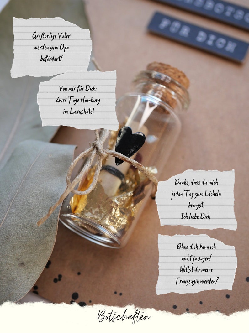 May include: A small glass bottle with a cork top is tied with twine and a black heart charm. The bottle contains a rolled up piece of paper and gold leaf. The bottle is sitting on a brown surface with a piece of paper that says "Danke, dass du mich jeden Tag zum L&auml;cheln bringst. Ich liebe Dich." and another piece of paper that says "Ohne dich kann ich nicht ja sagen! Willst du meine Trauzeugin werden?"